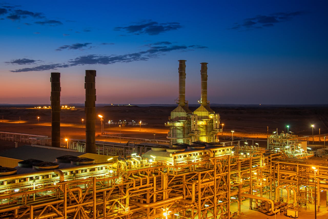Aerial view of an illuminated factory with chimneys at sunset, showcasing industrial architecture.